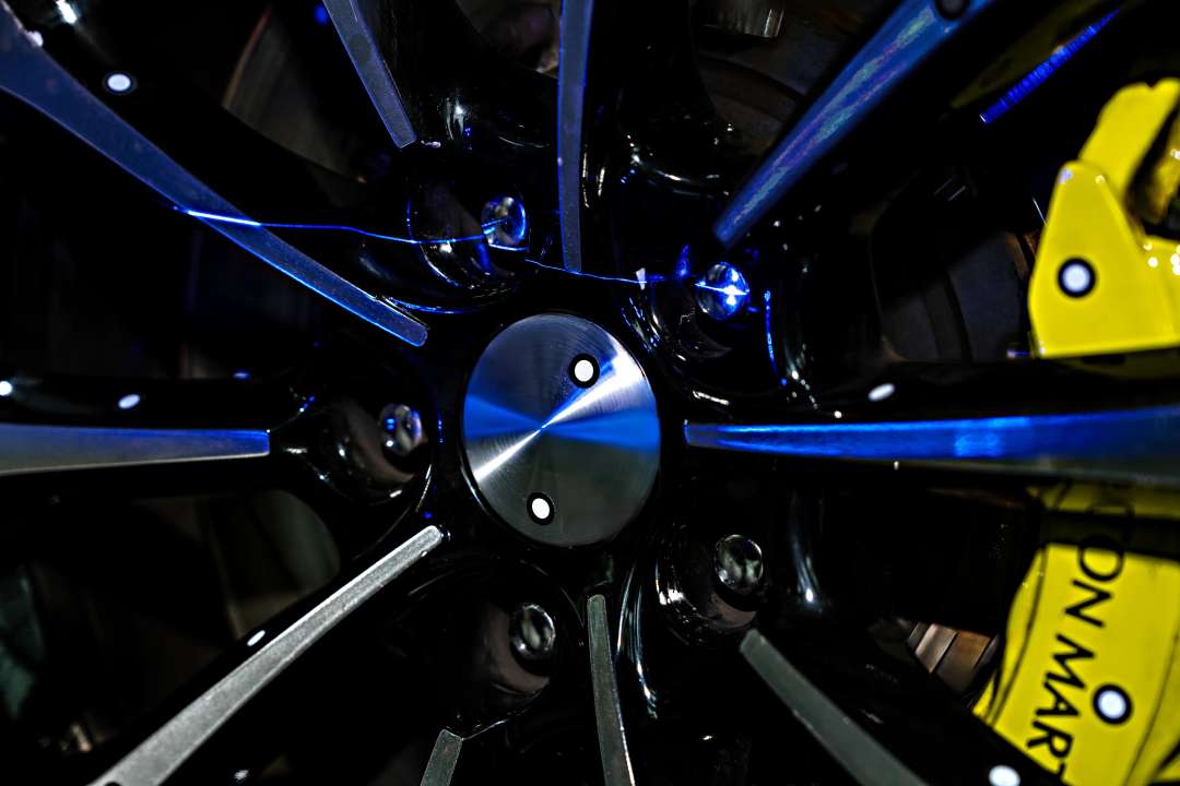 Líneas láser azules sobre una llanta de fundición negra y una pinza de freno amarilla durante el escaneado 3D