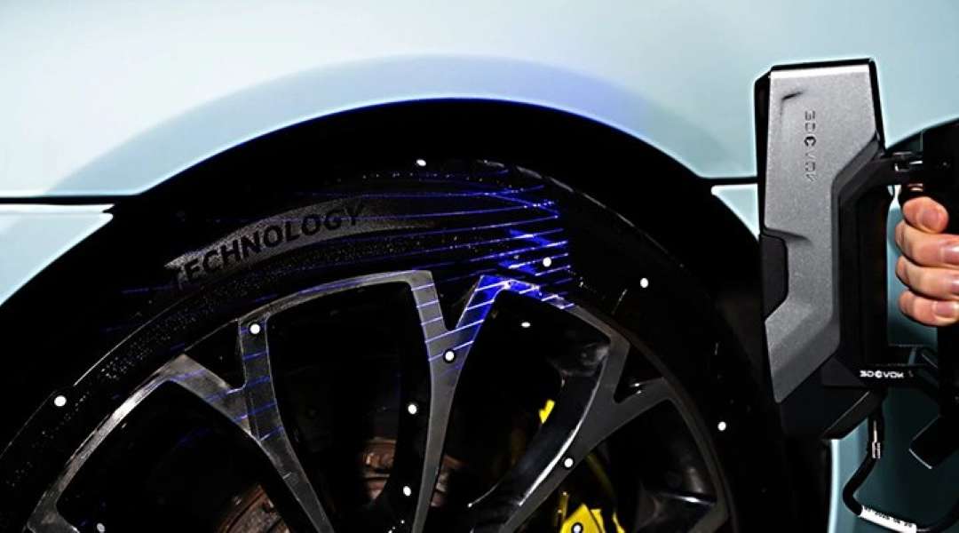 El escáner 3D de mano proyecta líneas láser azules sobre una rueda de automóvil con neumático; en la superficie se ven puntos marcadores blancos