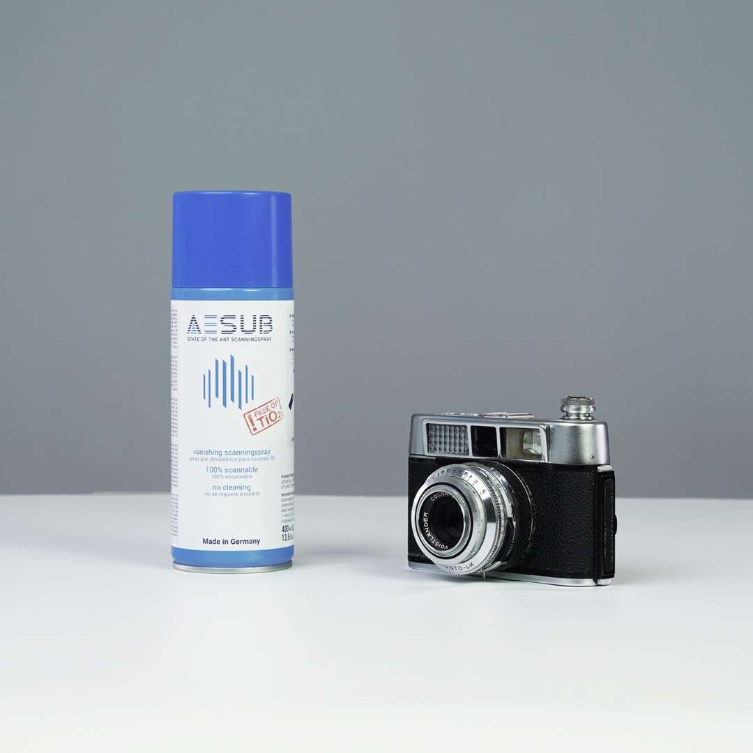AESUB Blue 400 ml spray can next to an untreated vintage camera — illustrating an uncoated reflective object before 3D scanning surface preparation