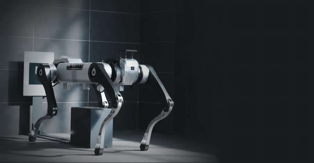 Robot con cuerpo cilíndrico plateado y articulaciones de las patas negras, de pie en una habitación embaldosada con poca luz