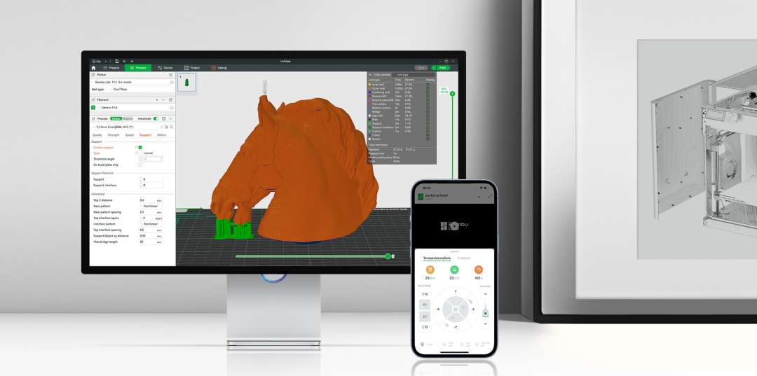 Monitor con la ventana de un laminador donde un modelo naranja de cabeza de caballo tiene soportes verdes; al lado, un móvil con la pantalla de control de la impresora.