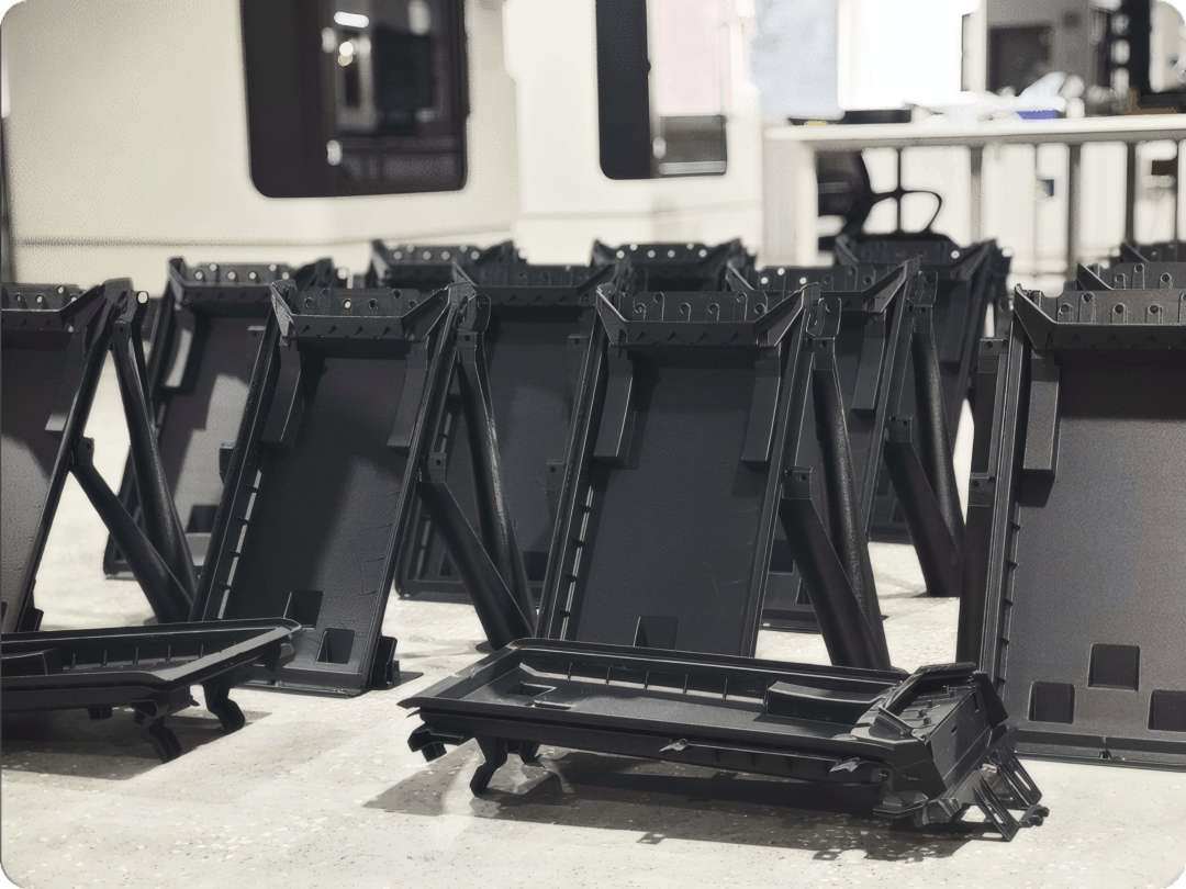 Piezas de plástico negro de gran tamaño y forma compleja colocadas en el suelo de una sala de producción