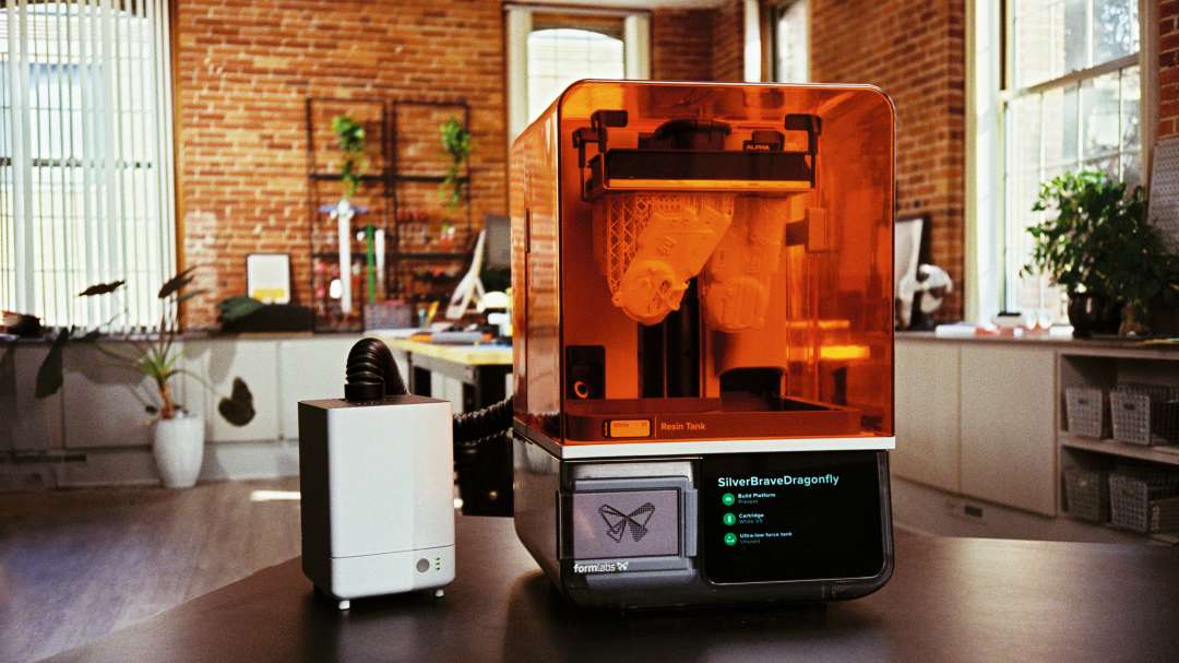 Dispositivo blanco con manguera flexible junto a una impresora 3D de resina con tapa naranja