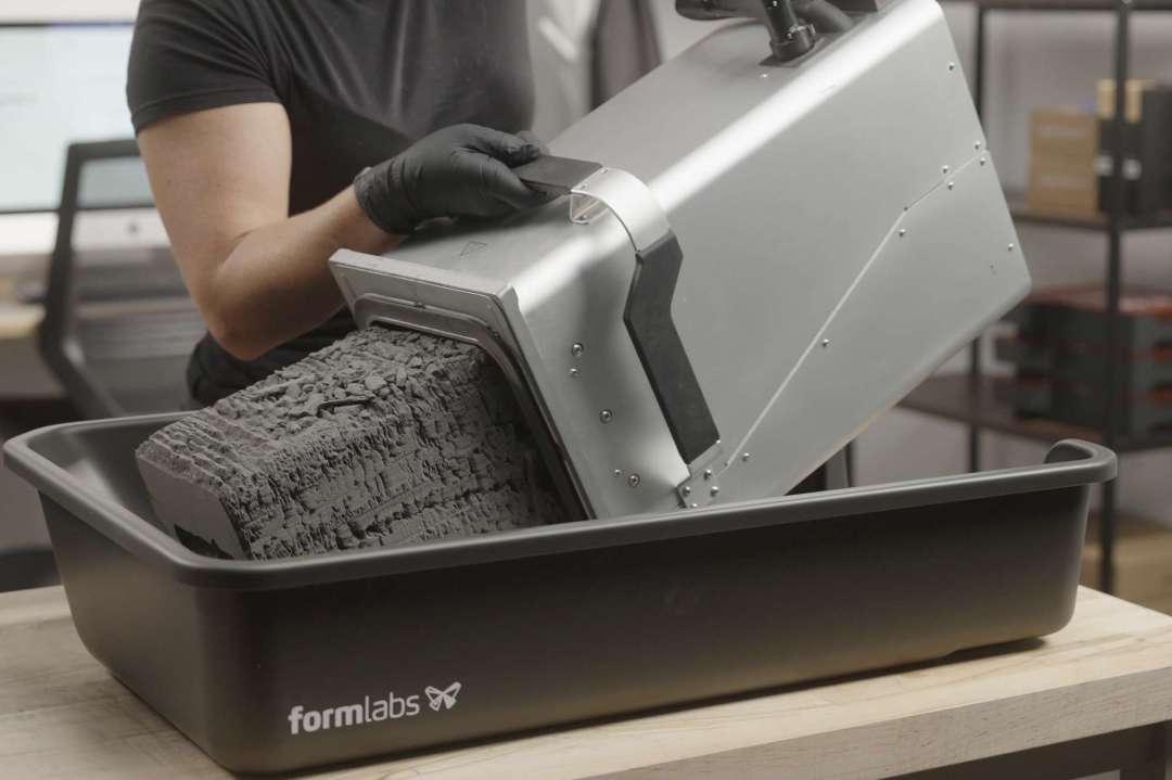 Bloque de polvo SLS deslizándose fuera de la cámara de fabricación hacia la bandeja del Fuse Depowdering Kit durante la extracción de piezas