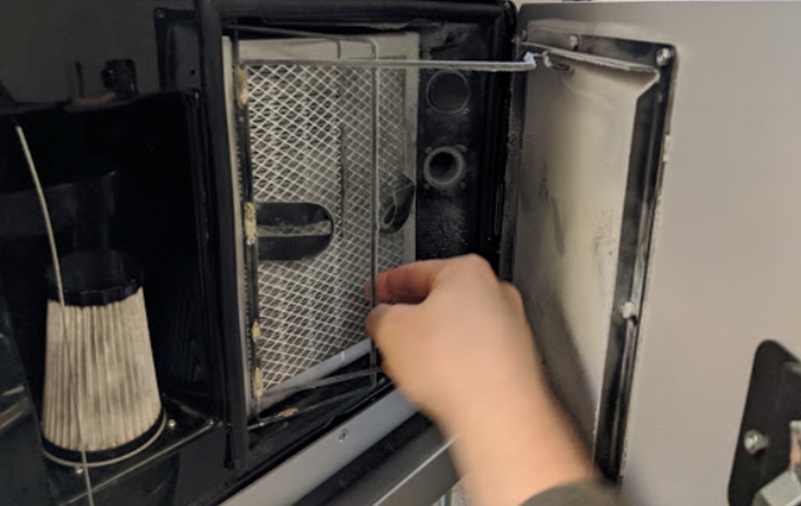 Mano desenganchando el gancho retendor inferior de la carcasa del filtro de escape del Fuse 1 durante el procedimiento de extracción