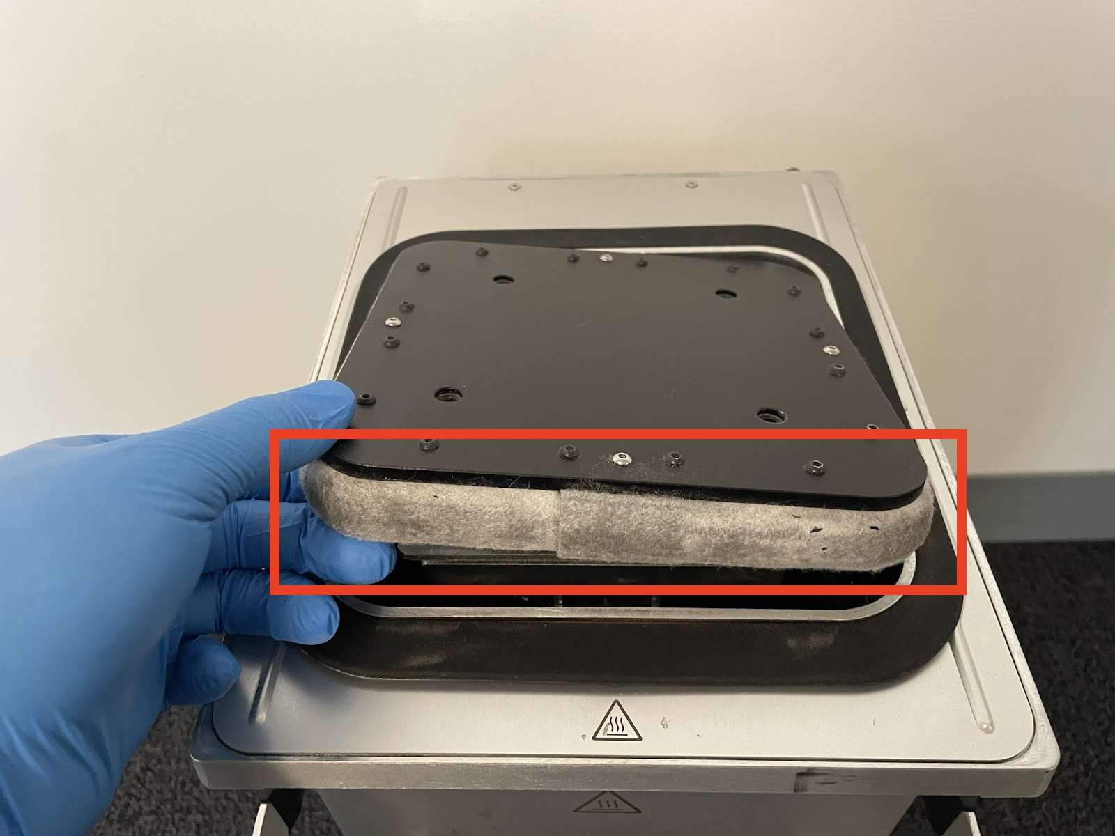 Cámara de fabricación de la generación Fuse 1 sujetada con guante mostrando el sello de fieltro alrededor de la plataforma de impresión resaltado en un rectángulo rojo