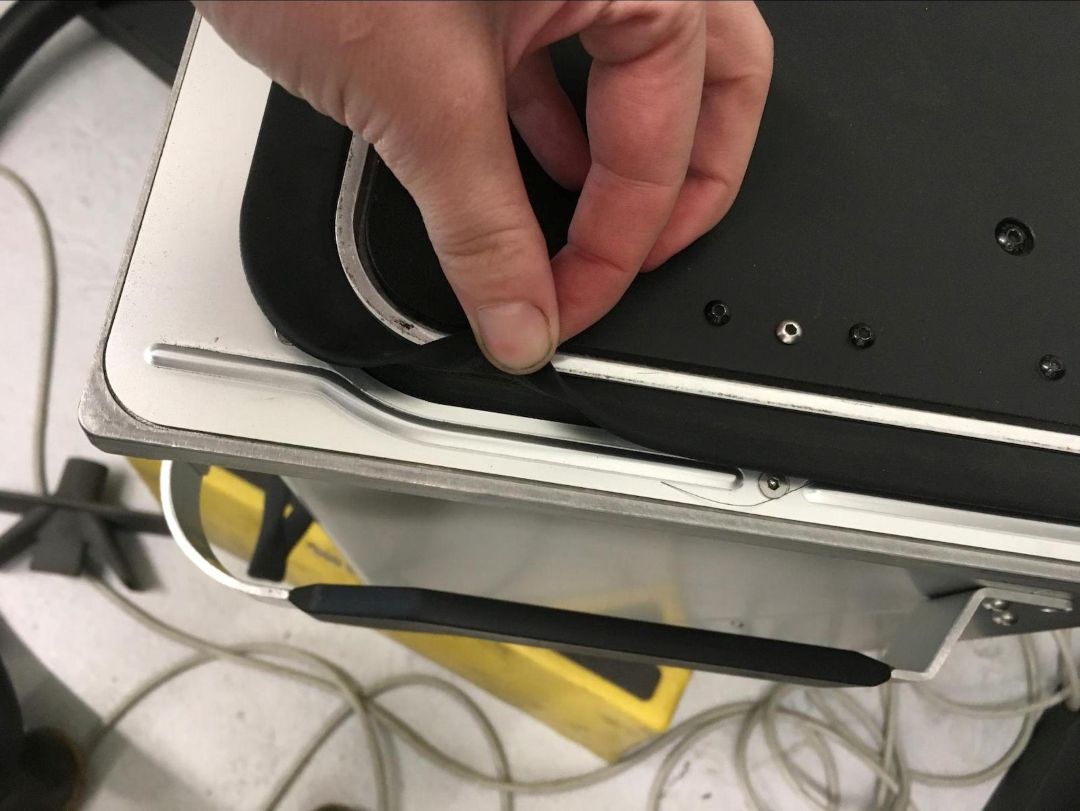 Mano levantando suavemente el borde exterior de la junta alrededor de la plataforma Fuse 1 para exponer la parte inferior durante una limpieza completa de cambio de polvo