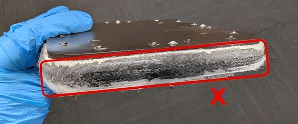 Mano con guante sosteniendo un segmento del sello de fieltro Fuse 1 con polvo SLS fundido e incrustado en todo el fieltro — marcado con X roja indicando que requiere sustitución