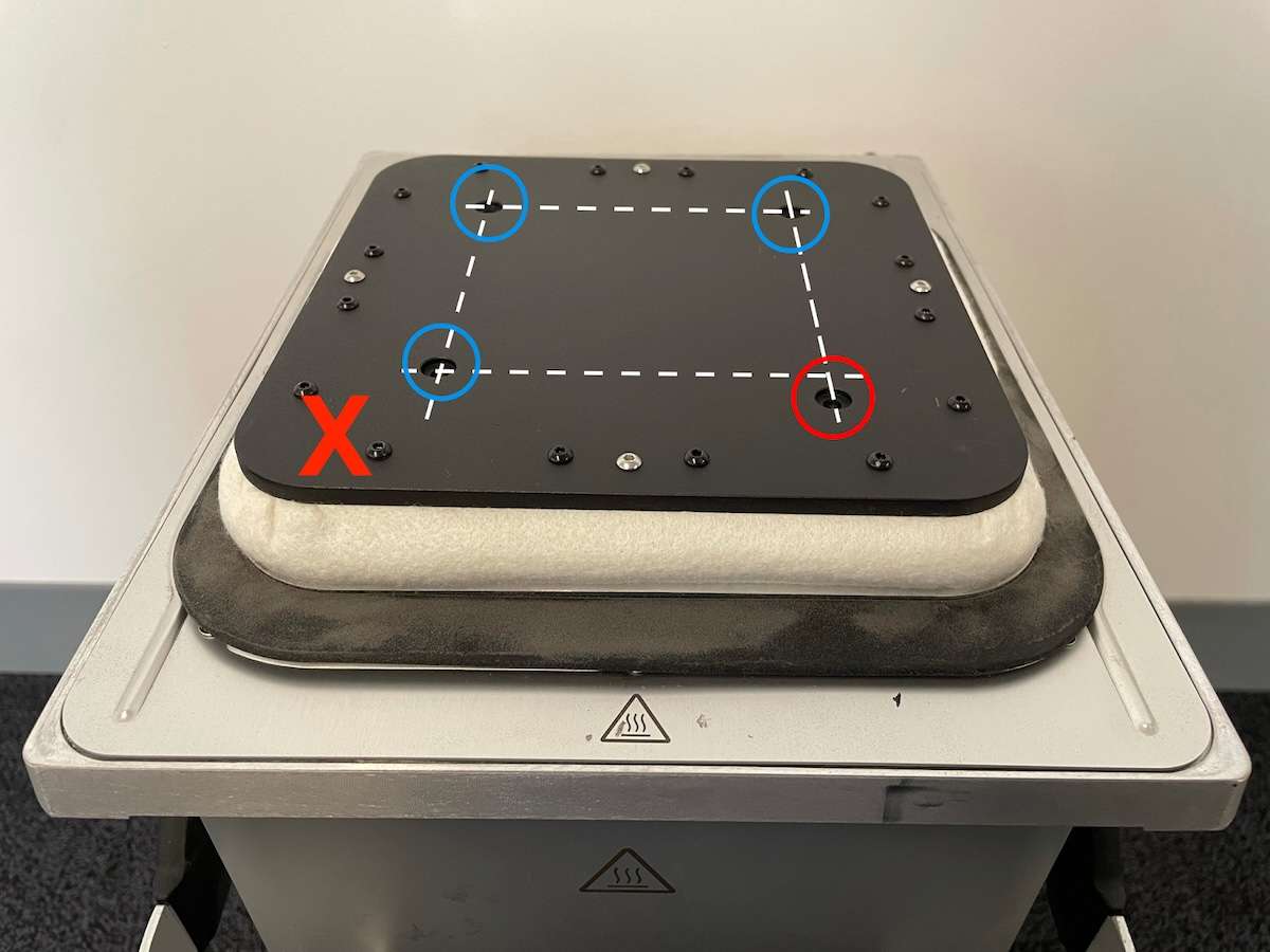 Plataforma de impresión de la cámara Fuse 1 en orientación incorrecta — X roja visible, un orificio de tornillo señalado en rojo mostrando la desalineación causada al girar la plataforma 90°