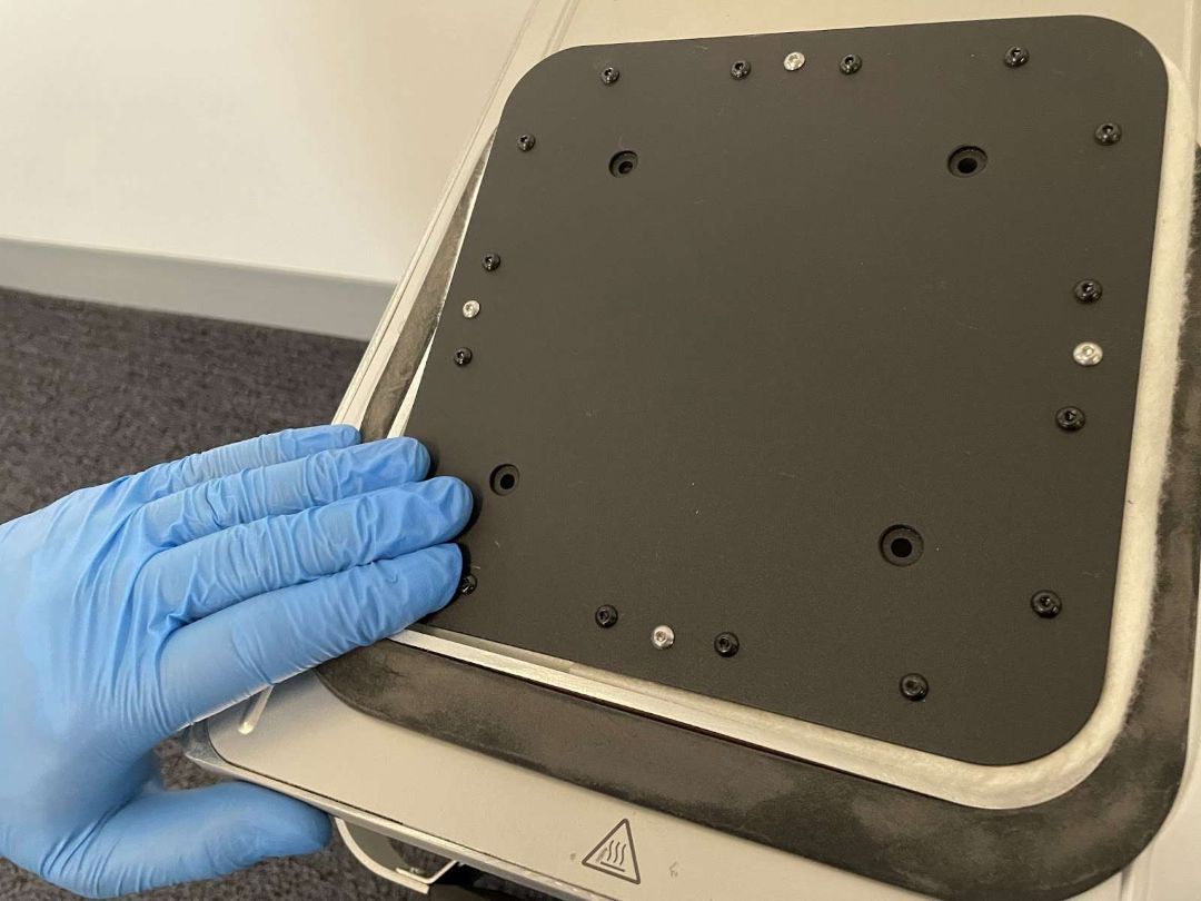 Mano con guante presionando una esquina de la plataforma de impresión Fuse 1 hacia la cámara de fabricación para asentarla contra el sello de fieltro