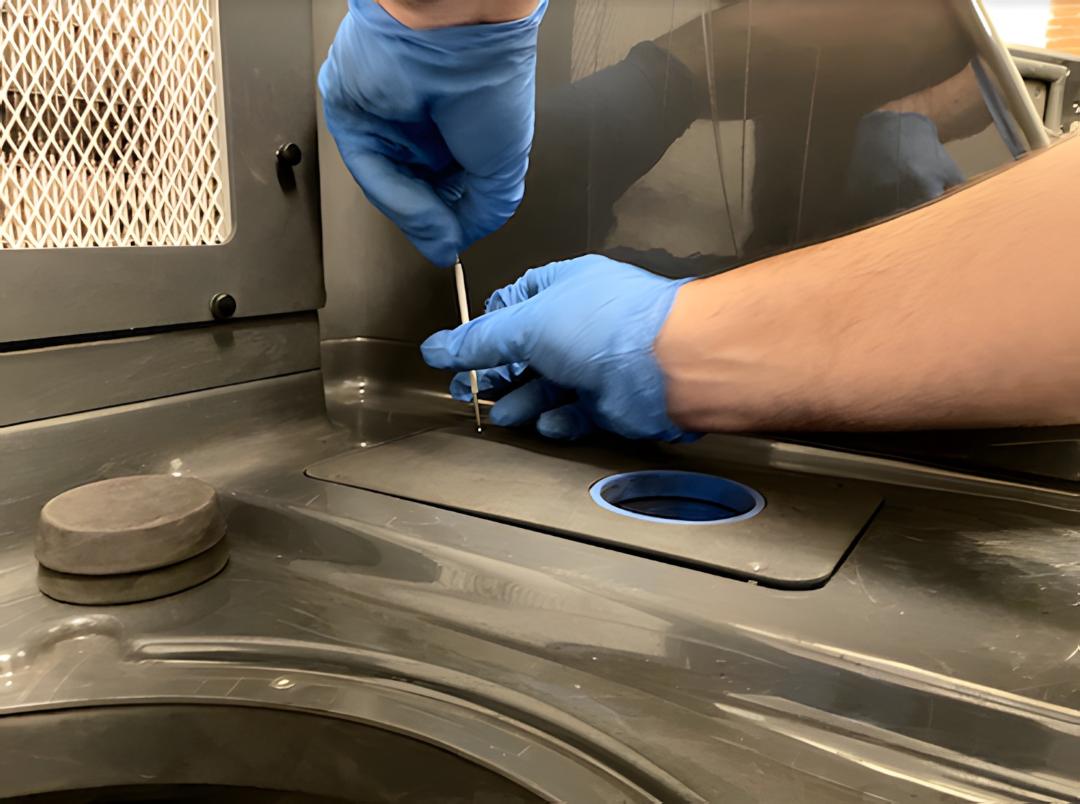 Técnico con guantes azules apretando tornillos hexagonales para instalar el Fuse Sift Funnel sobre la tapa de la tolva de polvo fresco del Formlabs Fuse Sift