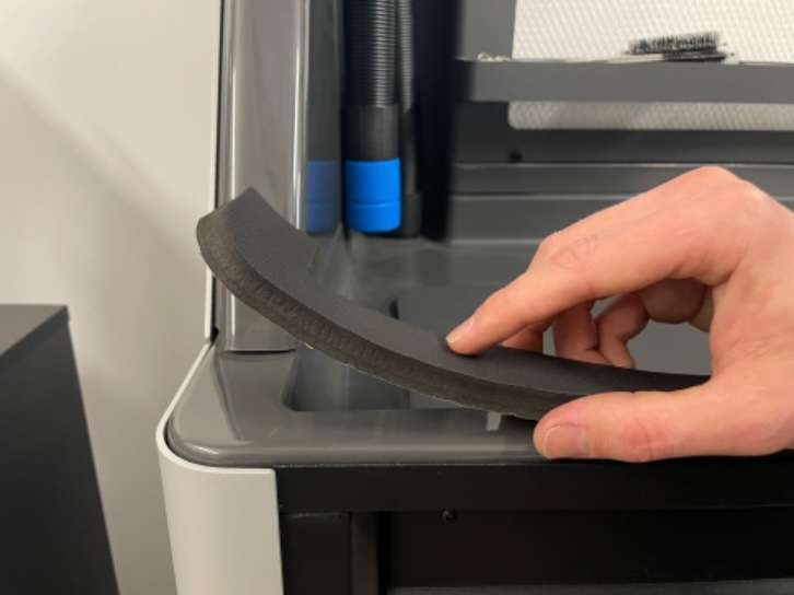 Mano despegando la junta de espuma adhesiva y presionándola sobre el labio frontal de la superficie de trabajo del Fuse Sift durante la instalación del Glovebox