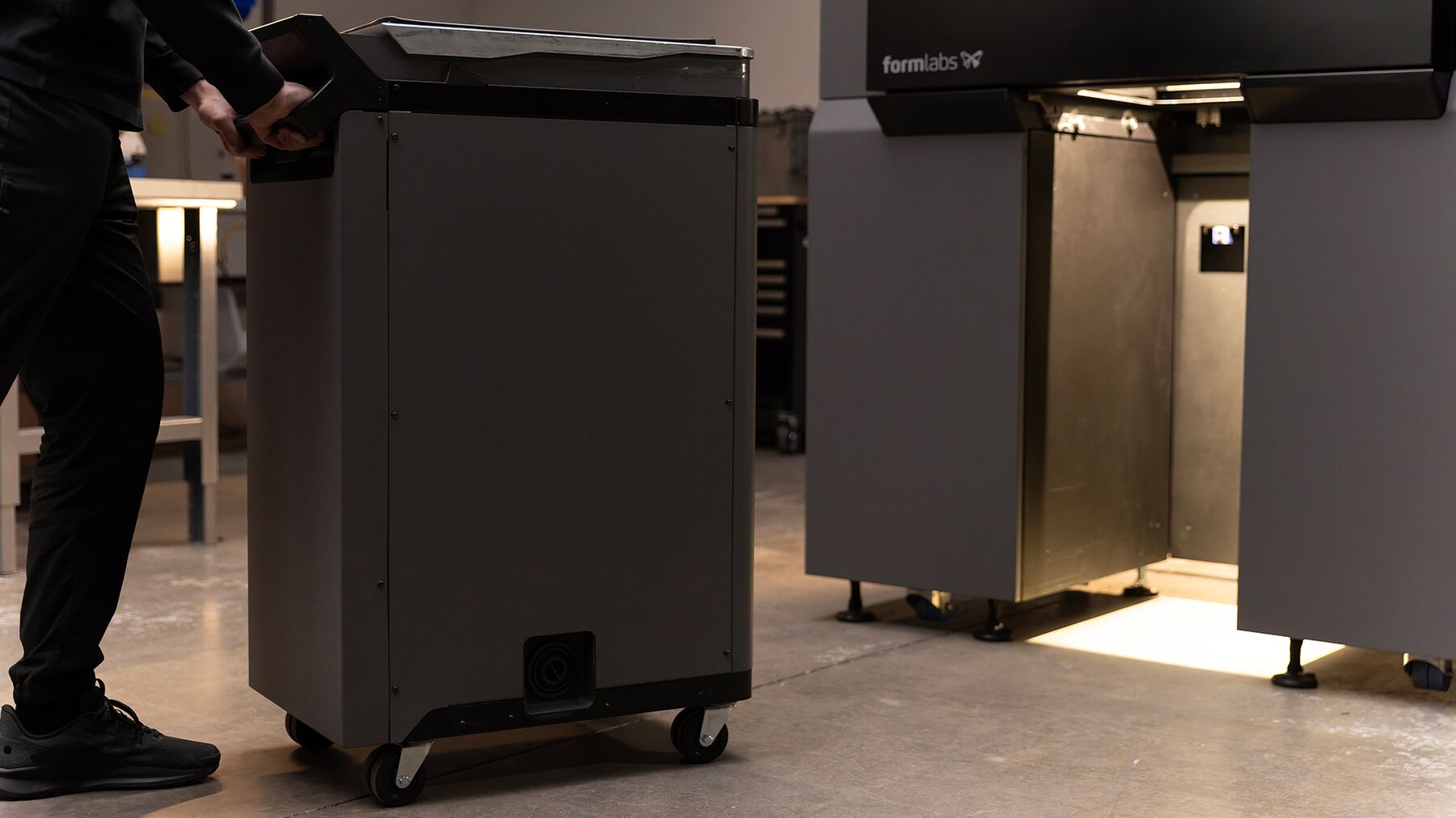 Un operador desplaza el módulo móvil hacia el compartimento abierto de la impresora Formlabs Fuse X1.