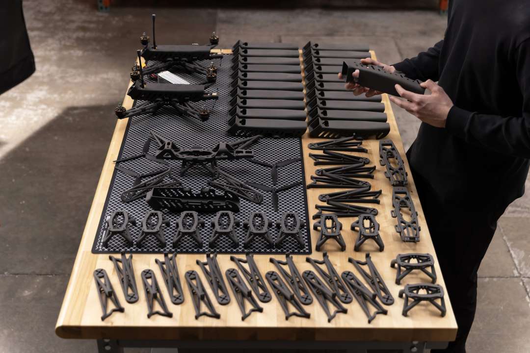 Componentes SLS desmontados de armação de drone — chassis, braços e elementos estruturais — dispostos sobre uma mesa de madeira