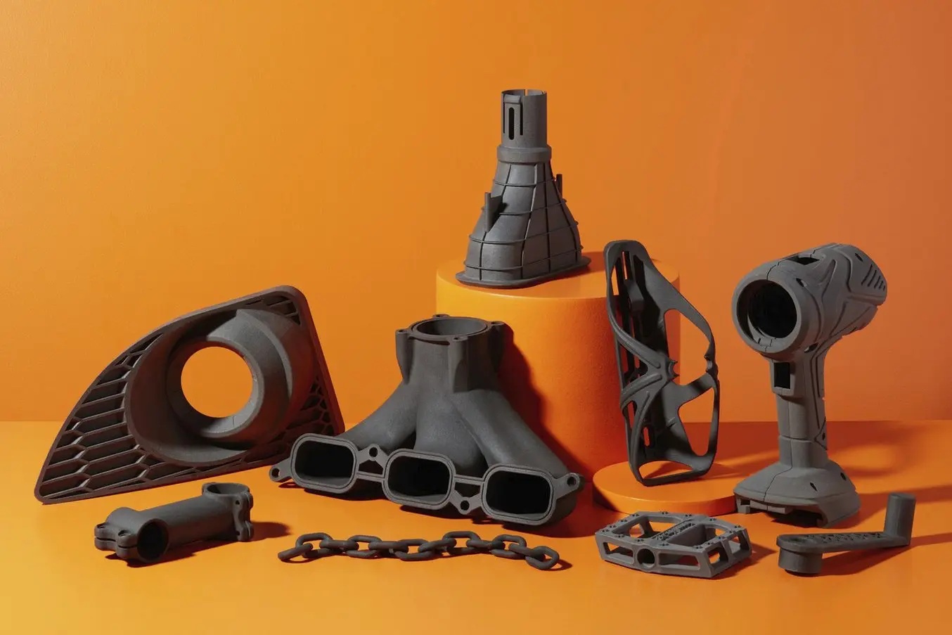 Piezas industriales de uso final en Formlabs Nylon 11 CF: rejilla de automóvil, colector de admisión, estructuras de celosía, cuerpo de taladro y pedales sobre fondo naranja