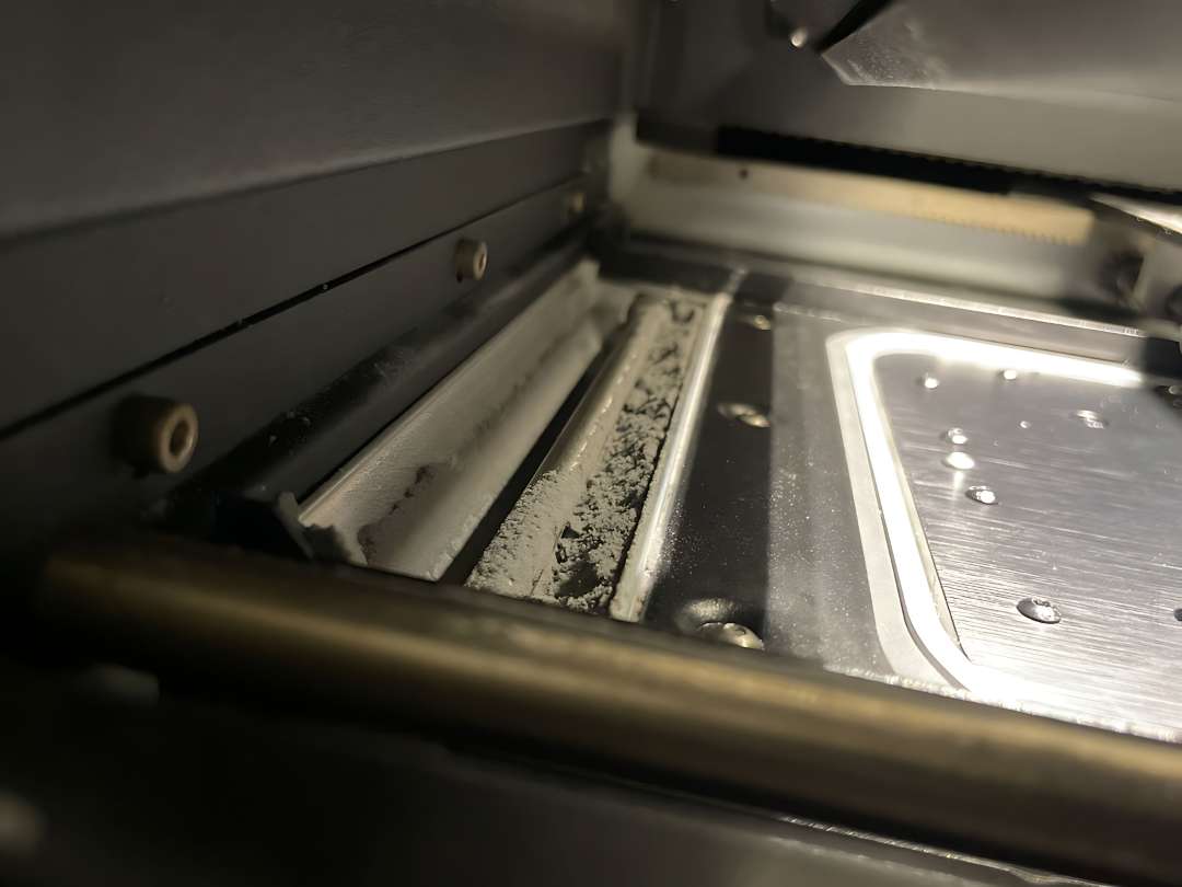 Primer plano del polvo Nylon 11 gris acumulado en el canal de la bandeja de la impresora Fuse 1 — requiere limpieza entre trabajos de impresión