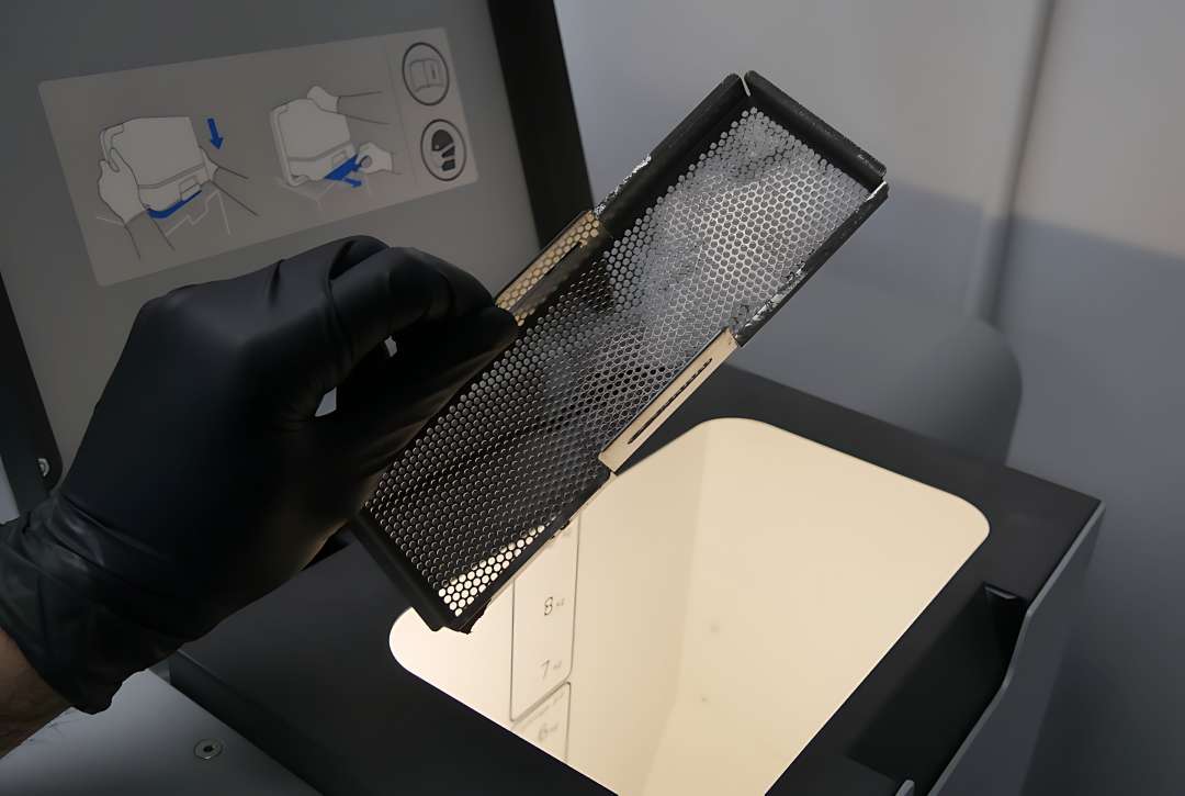 Mano enguantada retirando la trampa de residuos de malla de la tolva Fuse 1 antes de imprimir con Formlabs Nylon 11 Powder