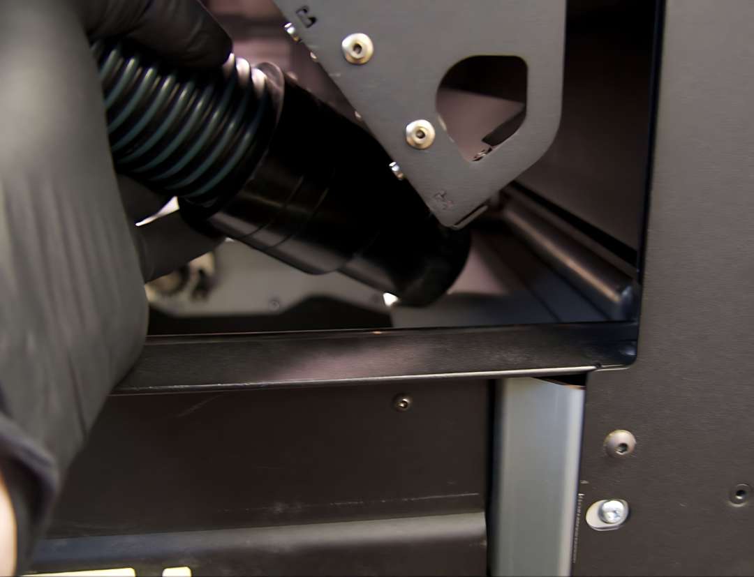 Mano enguantada usando la manguera de aspiradora para limpiar la bandeja de polvo derecha de la impresora Fuse 1 tras un trabajo de Nylon 11