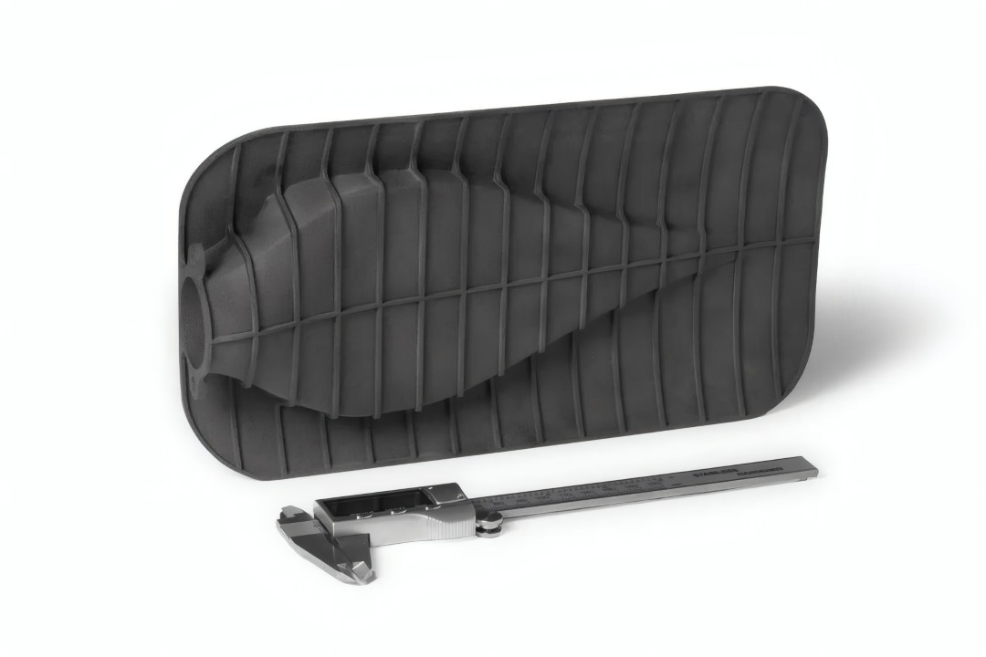 Conducto o protector térmico de gran tamaño para automoción impreso en Formlabs Nylon 12 GF Powder, mostrado con un calibre para referencia de escala