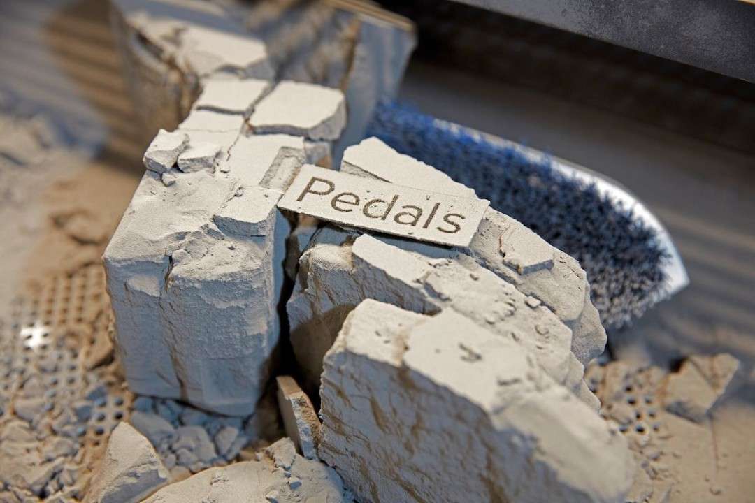 Extracción de piezas del bloque de polvo etiquetado 'Pedals' durante el posprocesado de piezas de Nylon 12 GF en el Fuse Sift