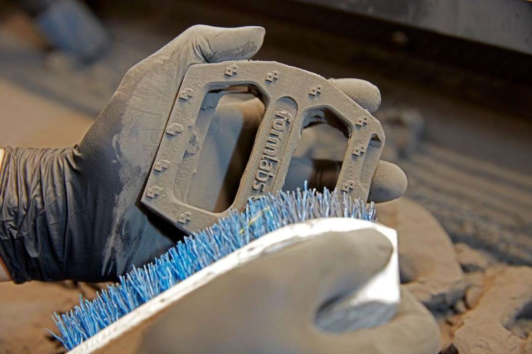 Cepillado del polvo SLS suelto de un pedal de bicicleta Formlabs durante el posprocesado de Nylon 12 GF en el Fuse Sift