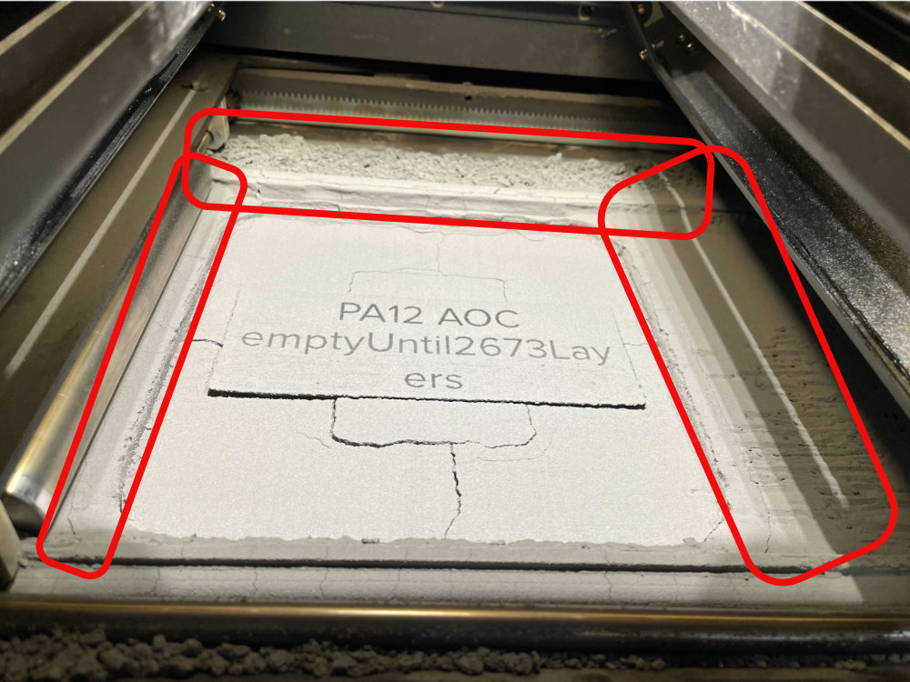 Cámara de construcción de la Fuse 1+ 30W abierta mostrando el cake de polvo PA12 AOC con los carriles superiores resaltados en rojo donde se acumula el Nylon 12 Tough