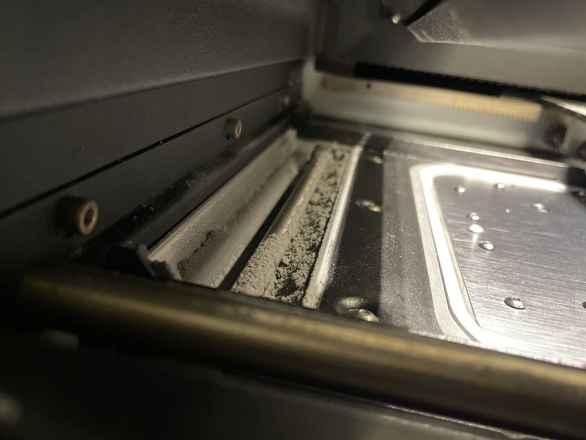 Primer plano del depósito de polvo de la Fuse 1+ 30W mostrando acumulación de polvo gris de Nylon 12 Tough en el raíl del depósito que requiere aspiración