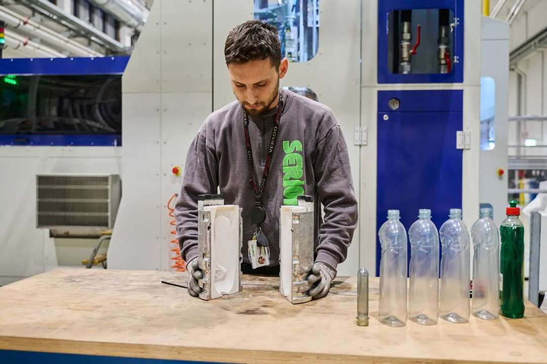 Un técnico extrae piezas de resina endurecida de las bandejas abiertas de la impresora, junto a botellas vacías para el posprocesado