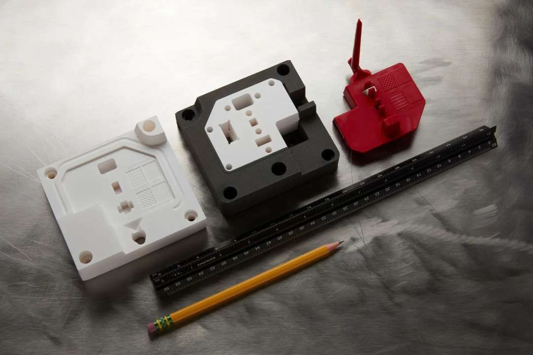 Tres prototipos impresos de carcasas de color blanco, gris y rojo junto a una regla y un lápiz como referencia de escala