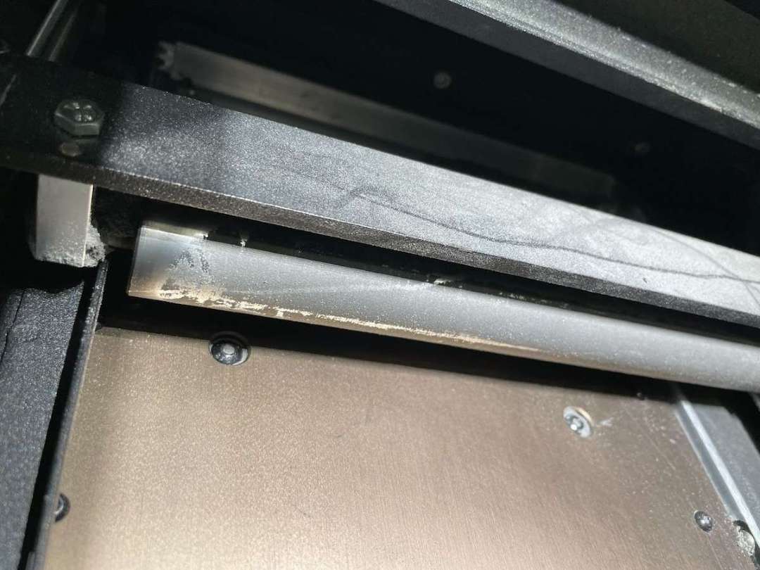 Primer plano de la acumulación de polvo TPU 90A semi-sinterizado en la hoja del recoater del Fuse 1 — requiere limpieza con etanol antes del siguiente trabajo