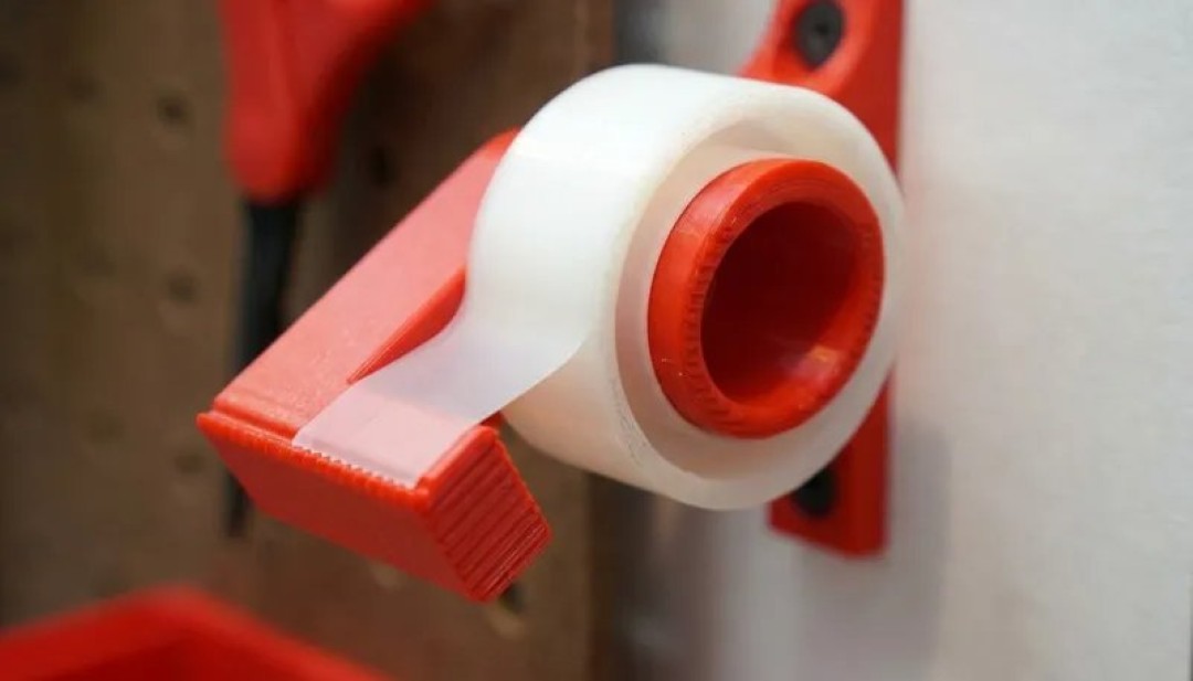 Dispensador de plástico rojo con un rollo de cinta adhesiva transparente en un panel perforado