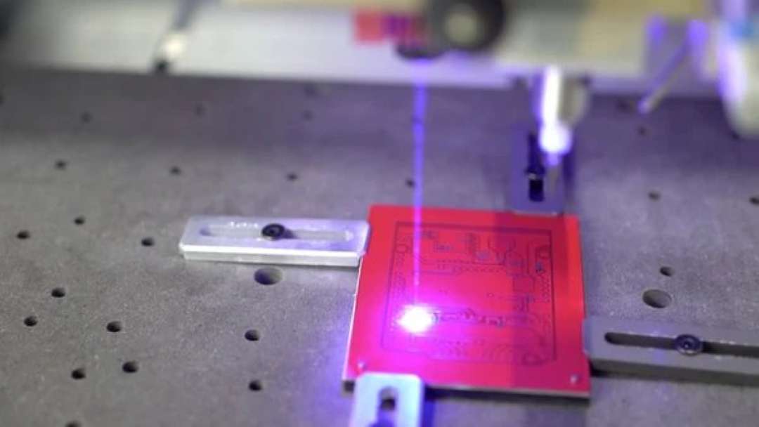 Módulo láser azul grabando el dibujo de un esquema sobre una placa roja en la mesa de trabajo de Carvera