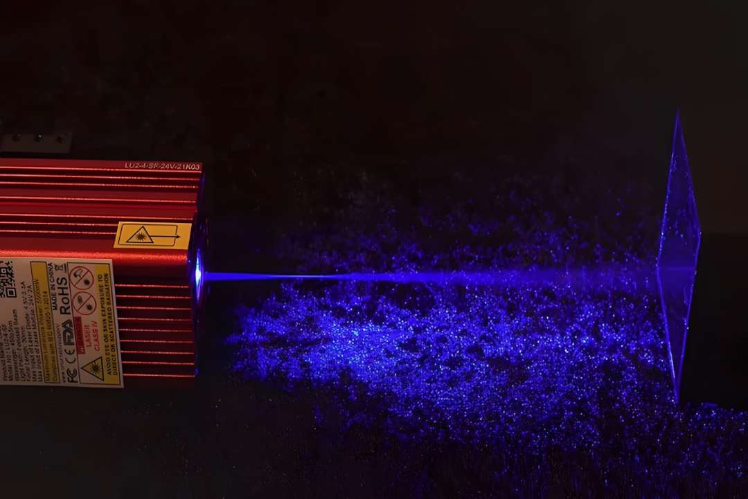 Ortur LU2-4-SF 5W laser module firing a vivid blue 450 nm beam toward transparent acrylic in a darkened environment, showing beam coherence