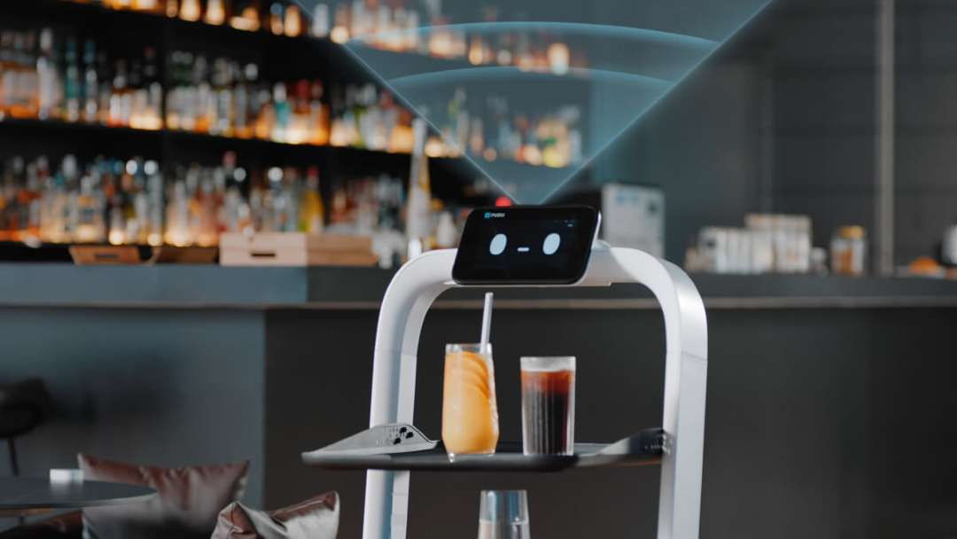 Robot PUDU PuduBot 2 repartiendo vasos de cóctel sobre una bandeja en un bar con poca luz, con el cono de detección del sensor VSLAM visualizado en azul sobre la cabeza del robot