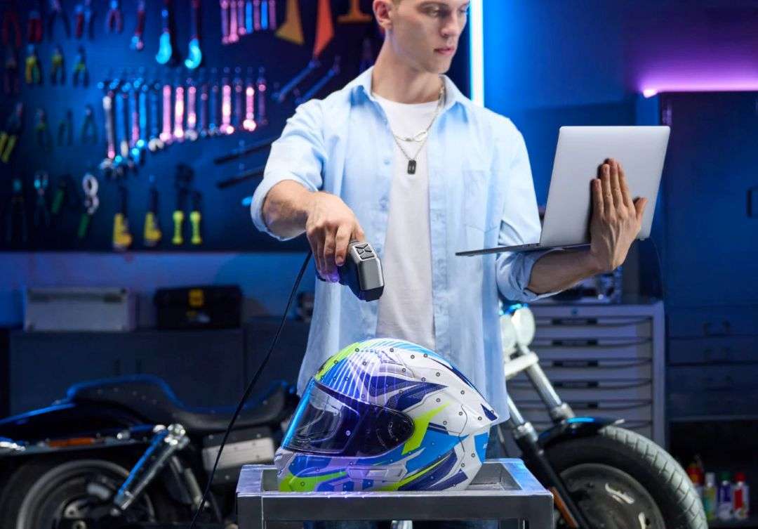 Un operador sostiene el escáner portátil sobre un casco de motocicleta, revisando los datos en un ordenador portátil en un taller