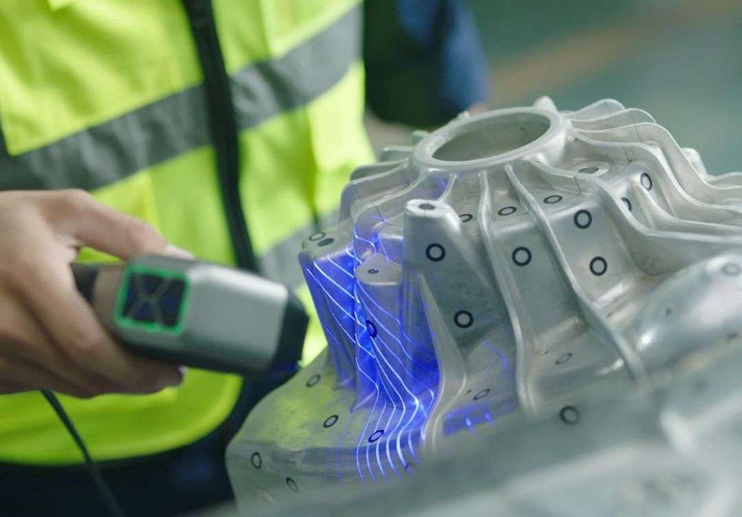 Escáner 3D manual que proyecta líneas láser azules sobre una pieza industrial metálica compleja con marcadores de seguimiento