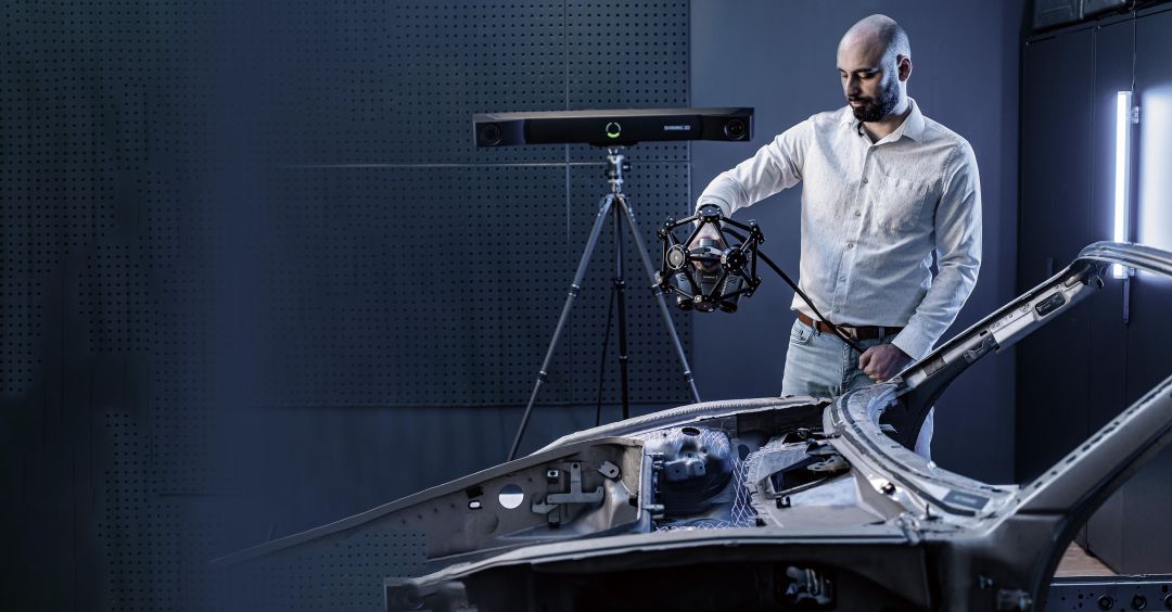 Operador sosteniendo el escáner portátil TE25 junto a la barra de seguimiento óptico FreeTrak sobre un trípode, escaneando un panel metálico automotriz sin marcadores