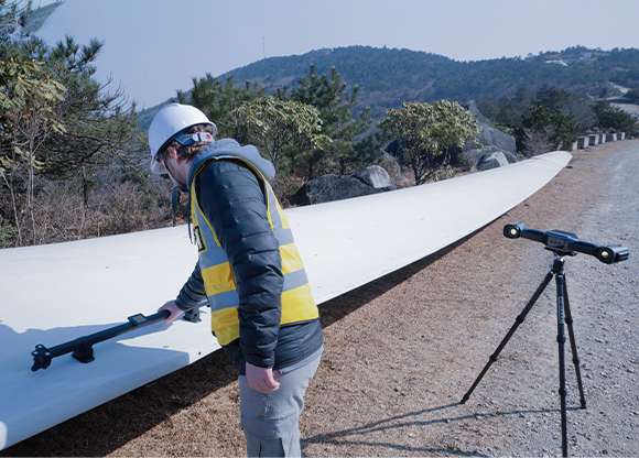 Ingeniero realizando mediciones fotogramétricas VPG en exteriores a lo largo de una pala de aerogenerador con FreeScan UE Nova en trípode