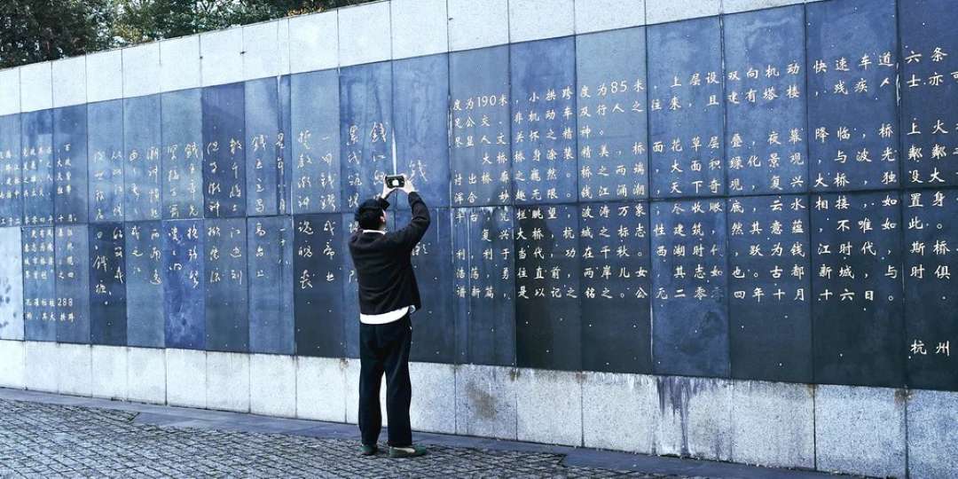 Persona de pie frente a grandes paneles de piedra oscura con inscripciones chinas en el exterior, documentando la superficie para su escaneo 3D