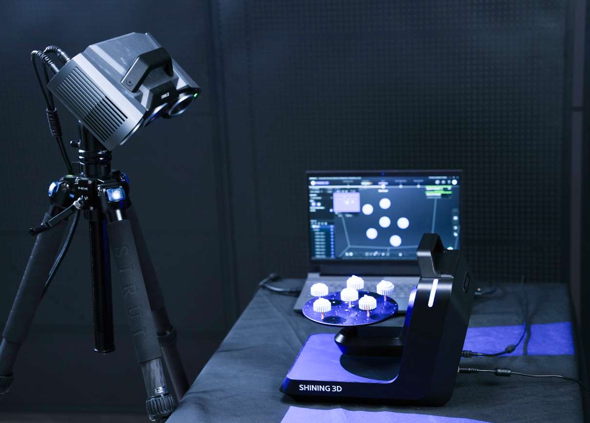 Primer plano del escáner OptimScan Q9 sobre la plataforma rotatoria de doble eje con piezas blancas tipo engranaje iluminadas por proyección LED azul