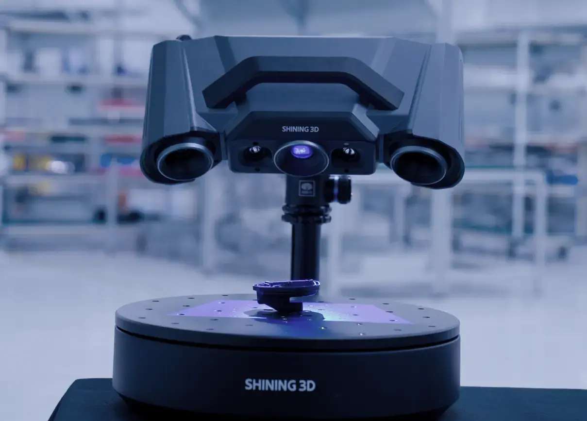 OptimScan Q9 montado en trípode con piezas pequeñas sobre una plataforma rotatoria adjunta que muestra la capacidad de doble rango de escaneo