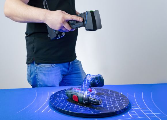 FreeScan UE Pro escaneando un taladro sobre una plataforma giratoria, con múltiples líneas de láser azul proyectadas sobre el objeto en modo de escaneo múltiple