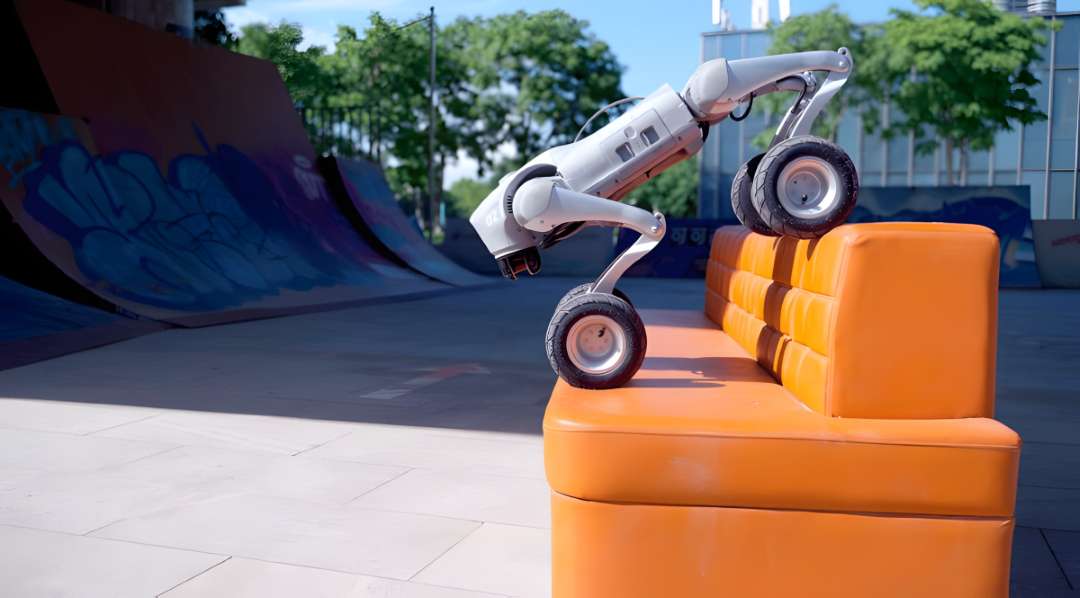 Robot Unitree Go2-W escalando sobre un obstáculo acolchado de color naranja en un skatepark, con las patas delanteras elevadas mientras los neumáticos traseros proporcionan empuje desde el suelo