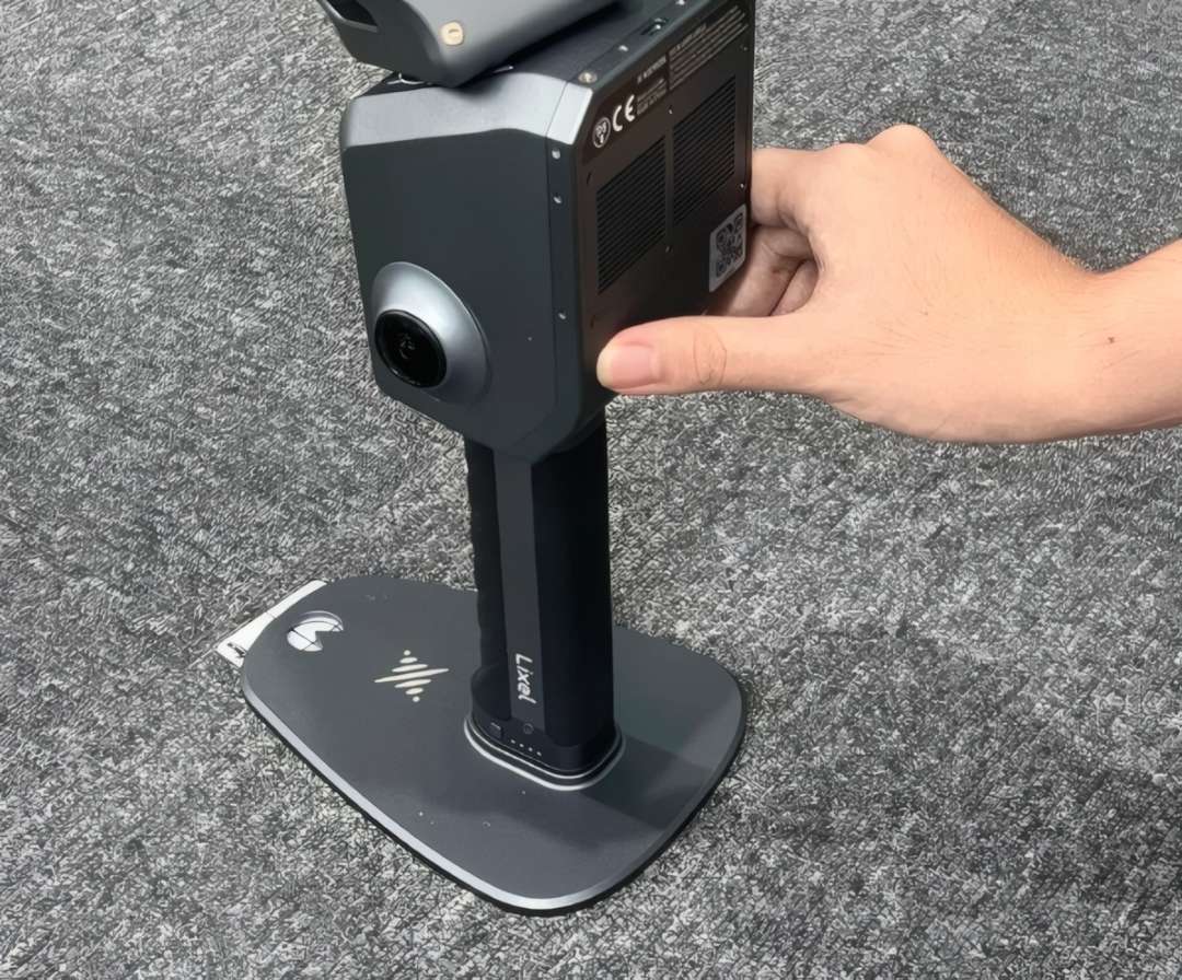 Mano sosteniendo el escáner 3D de aluminio Lixel 2 Pro, de pie sobre una placa base plana