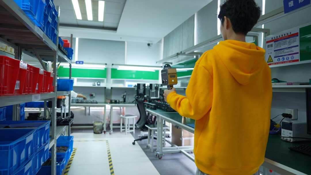 Vista desde atrás: persona con ropa amarilla sosteniendo el dispositivo en el interior de una instalación industrial rodeada de estanterías