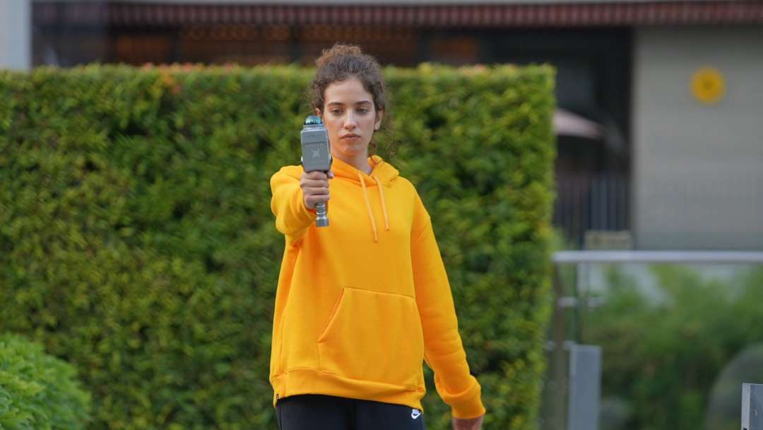 Vista frontal: operadora con sudadera amarilla caminando por un patio abierto con el escáner en mano