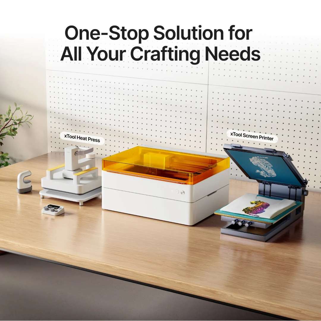 xTool M1 Ultra positioned on a studio workbench between the xTool Heat Press (left) and the xTool Screen Printer (right), showing a complete one-stop textile and craft customisation ecosystem