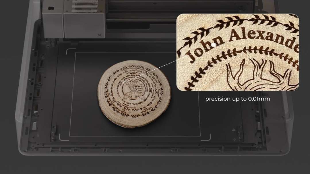 Close-up of laser-engraved wooden disc inside xTool M1 Ultra — magnified inset reveals fine lettering and decorative linework with precision up to 0.01 mm