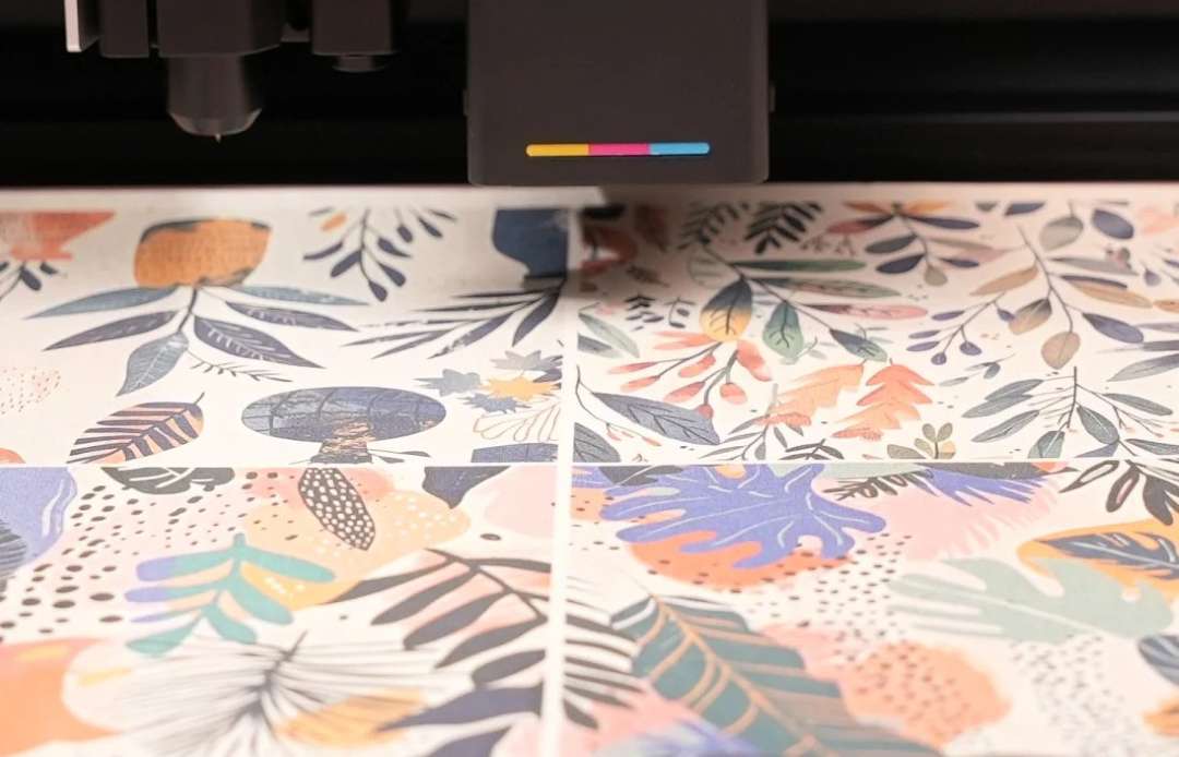 xTool M1 Ultra inkjet module printing a vibrant multicolour tropical leaf and botanical pattern directly onto a substrate — CMY colour bar visible on the print head